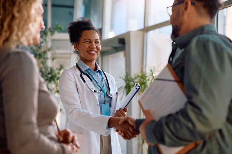 Happy African American doctor greeting a man who came with his wife for medical appointment at the clinic