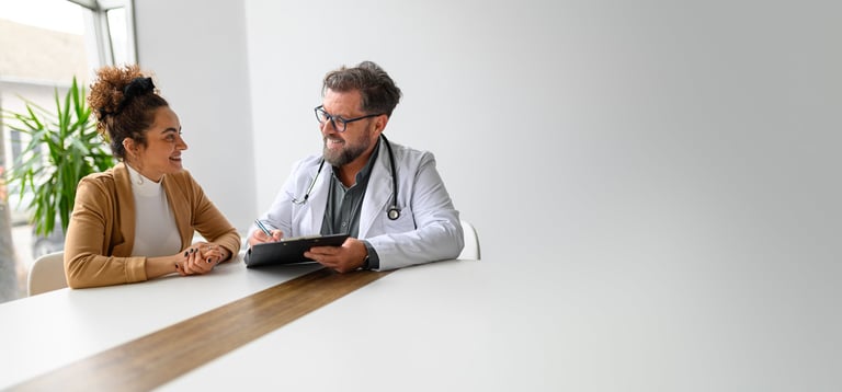 Professional male doctor talking to female patient at desk in hospital